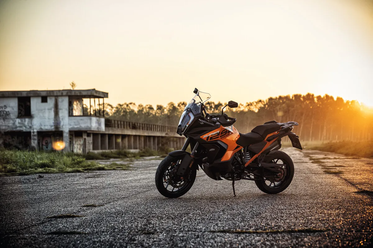 KTM 1290 Super Adventure S grise et orange à l'arrêt sur une route au soleil couchant