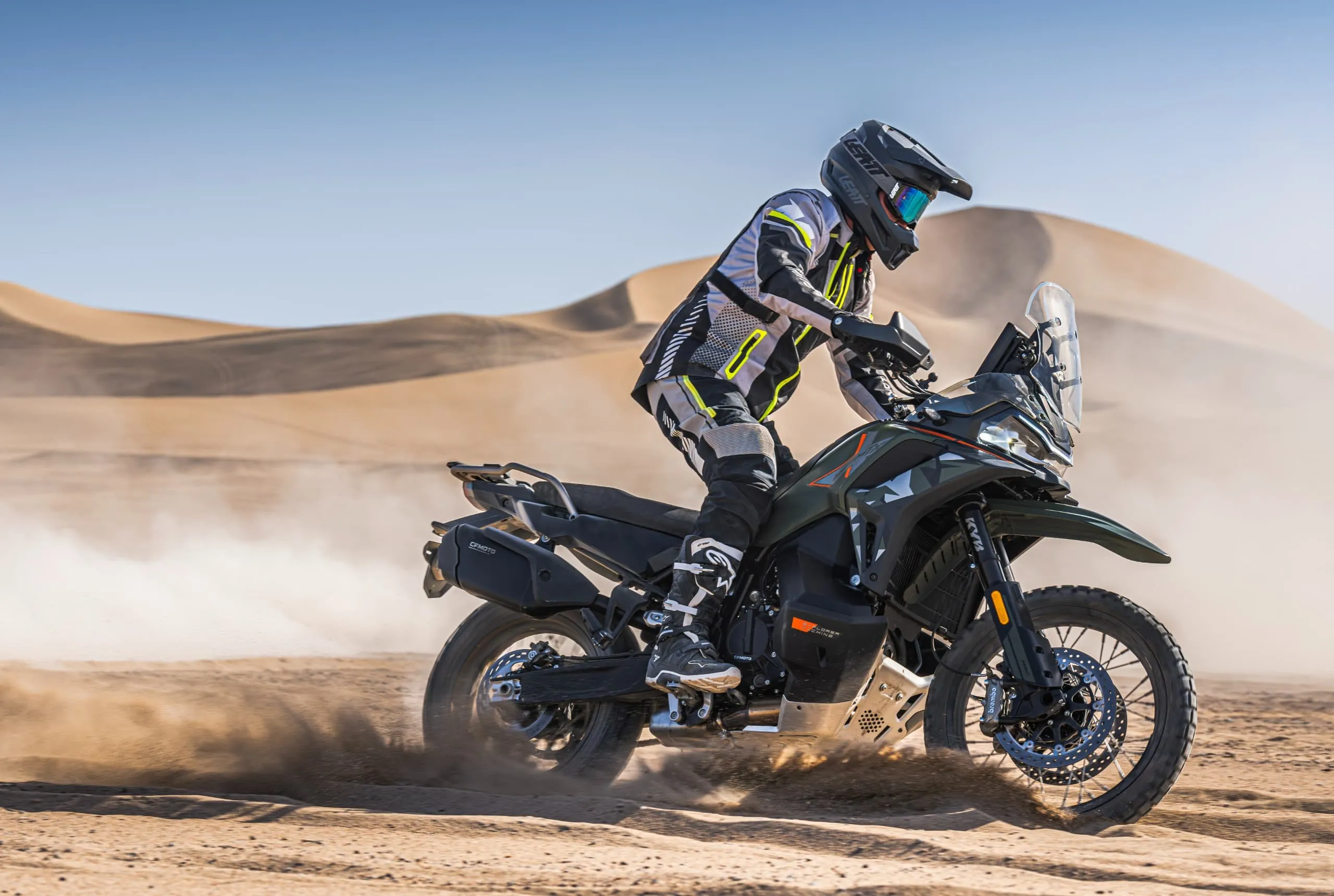 CFMoto 1000MT-X en action sur une dune de sable, pilote debout sur les repose-pieds