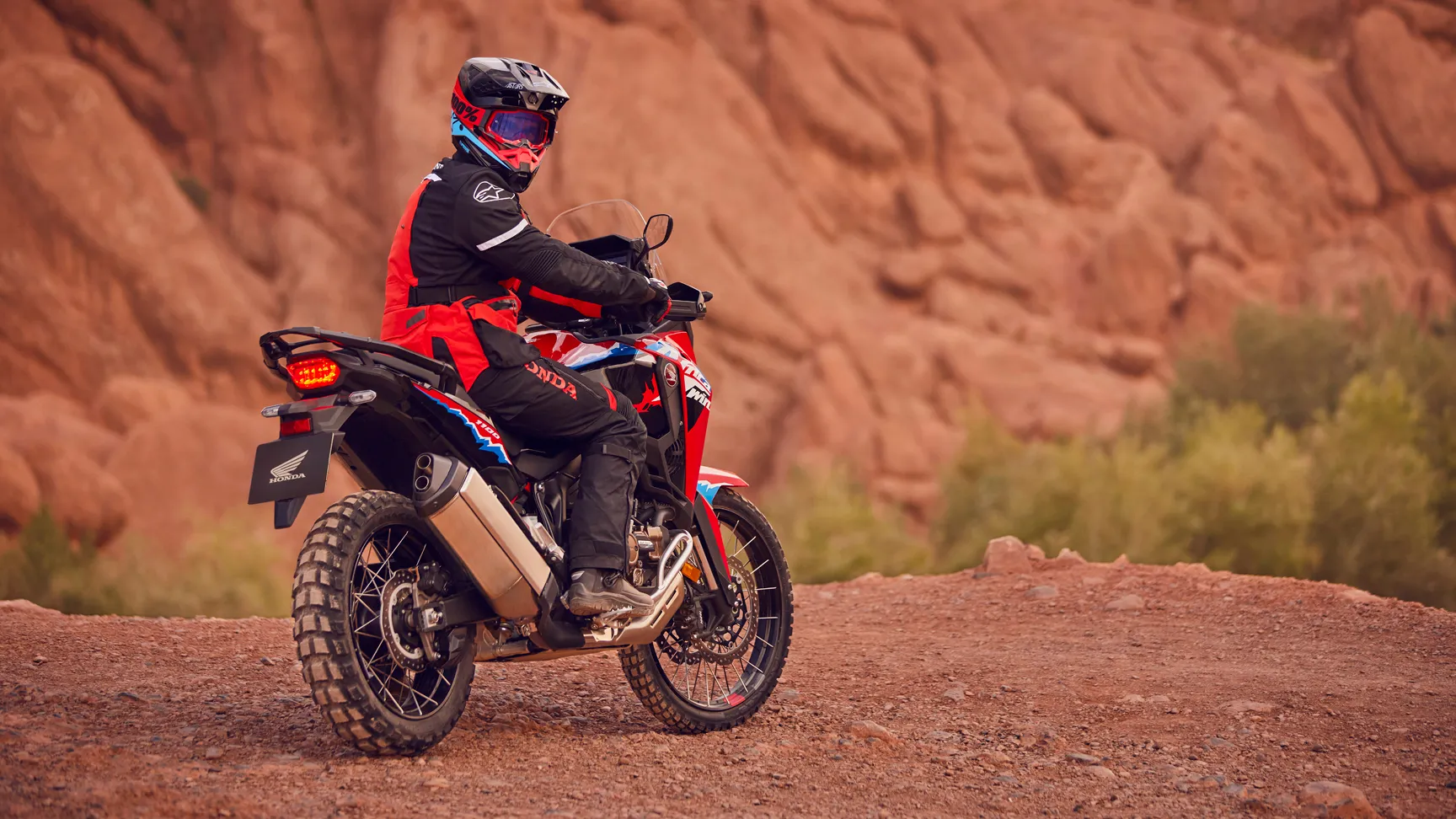 Honda CRF1100L Africa Twin en action sur un terrain rocheux ocre, pilote debout sur les repose-pieds