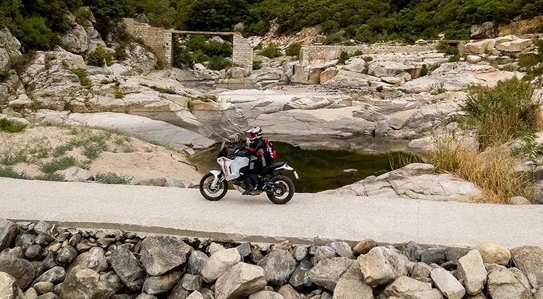 Ducati DesertX V2 en situation sur un terrain de pierres, au bord d'un cours d'eau